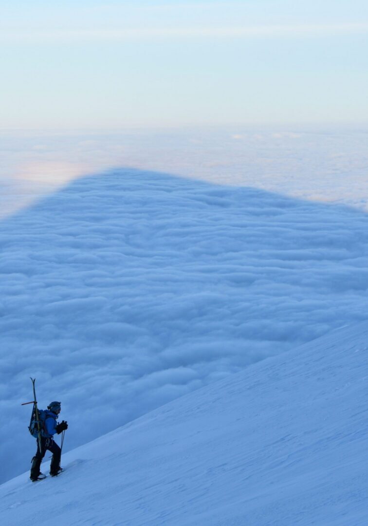 Mountaineer ascending snowy slope above sea of clouds